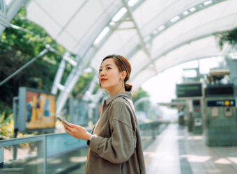 Confident young Asian businesswoman using smartphone while waiting for the train in subway station. Commuting to work. Travelling on public transportation in the city. Technology in everyday life. Business on the go