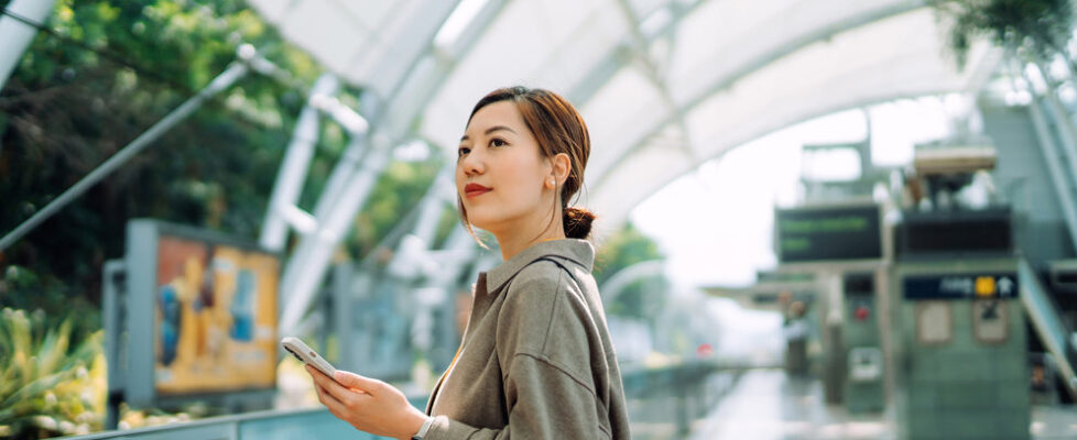 Confident young Asian businesswoman using smartphone while waiting for the train in subway station. Commuting to work. Travelling on public transportation in the city. Technology in everyday life. Business on the go